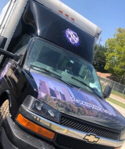 A black truck with a logo on its front and sides reads "TG Painting Co." The front also features a graphic of city buildings.