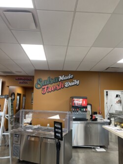 Image of a food service area with signage reading "Salsa Made Fresh Daily." There are a soda fountain, a sign directing customers, and a nearby restrooms sign.