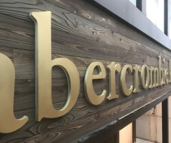 Close-up image of the Abercrombie & Fitch storefront signage, featuring large gold letters on a wooden background.