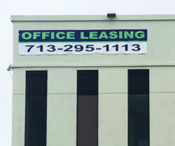 A building with a large sign for office leasing, displaying a contact number: 713-295-1113.