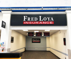 Entrance to a Fred Loya Insurance office with signs advertising no hidden fees, immediate insurance while shopping, and first month starts policy. Restroom signs are visible on the left.