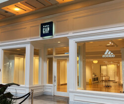 A storefront with a Baby Gap sign above the entrance, featuring large display windows. The adjacent store, Adidas, is also visible with a portion of its sign and logo.