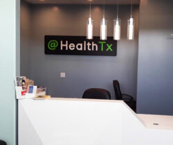 A medical reception desk with a sign that reads "@ HealthTx" on the wall and pamphlets on the countertop.