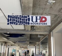 A hallway with a sign reading "UHD Bookstore" hanging from the ceiling. The ceiling features exposed ductwork, and people are visible in the distance.