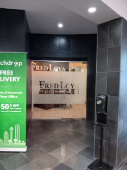 Entrance to a Fred Loya Insurance office with a sign indicating free delivery from a food service, and a hand sanitizer dispenser by the door.
