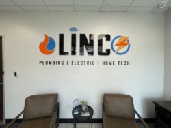 Office lobby with two chairs, a small table, and a wall-mounted sign that reads "Linc Plumbing | Electric | Home Tech.