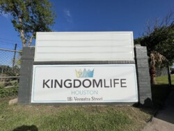 A sign for "Kingdom Life Houston" at 18 Veenstra Street is displayed on a brick structure with trees and a fence in the background.