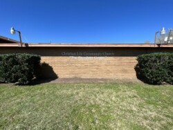 A brick building with a sign that reads "Christian Life Community Church 'The Freedom Center'" above two bushes under a clear blue sky.