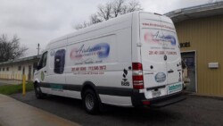 A white Airstream Air Conditioning and Heating service van is parked outside a building. The van has the company's contact information and slogan printed on its sides and rear.