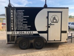 A white and black trailer with a list of handyman services including carpentry, painting, plumbing, and more. The trailer features a company logo, contact number, and website.